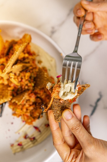 Fatma delicately places cultured and aged vegan cheese onto a cracker using a fork, creating a mouthwatering combination of flavors and textures